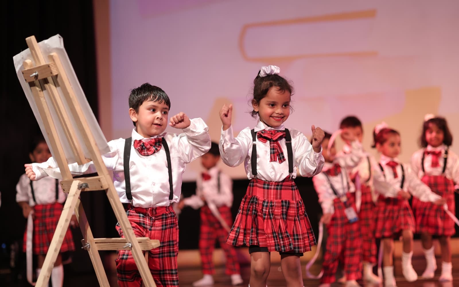 Young learners in matching plaid costumes performing on stage